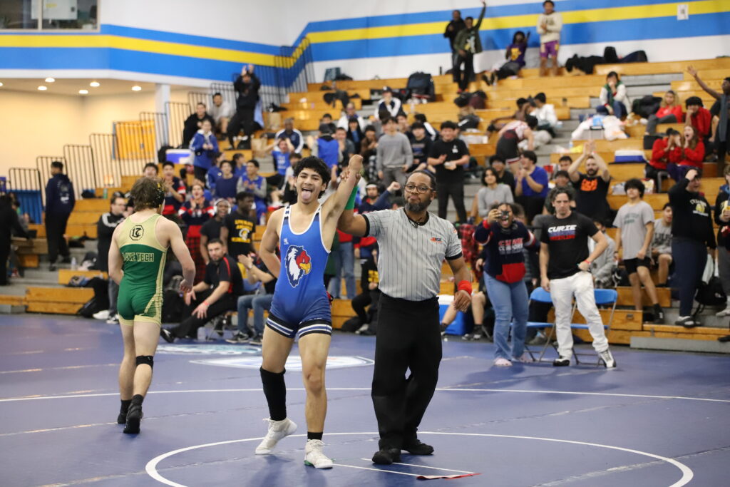 Curie wrestler Victor Quiroz celebrates a victory as the referee raises his arm